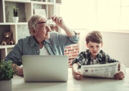 Generationen: Großvater am Laptop und Enkel mit der Tageszeitung