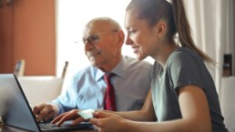Älterer Herr und junge Frau arbeiten gemeinsam am Laptop.