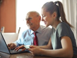 Älterer Herr und junge Frau arbeiten gemeinsam am Laptop.