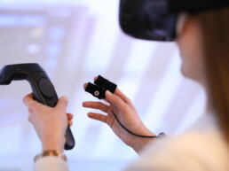Eine Frau hat eine VR-Brille auf und hält zwei Bedienteile in den Händen.