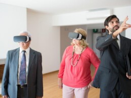 Ein älteres Ehepaar mit VR-Brillen lässt sich von einem Mann eine Wohnung zeigen.