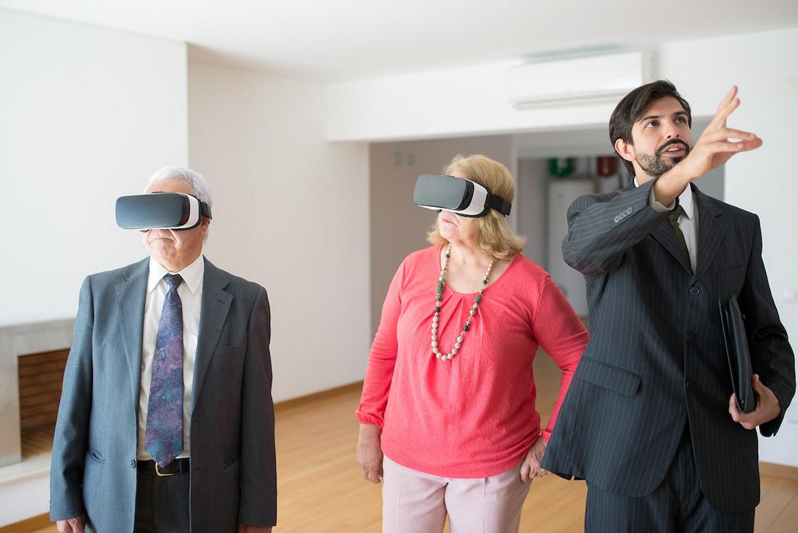 Ein älteres Ehepaar mit VR-Brillen lässt sich von einem Mann eine Wohnung zeigen.