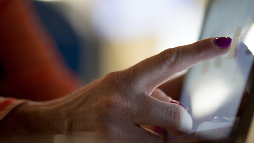 Der Finger einer älteren Frau tippt auf einem Tablet.