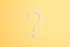 Ein Fragezeichen aus weißen Tabletten auf gelbem Hintergrund.