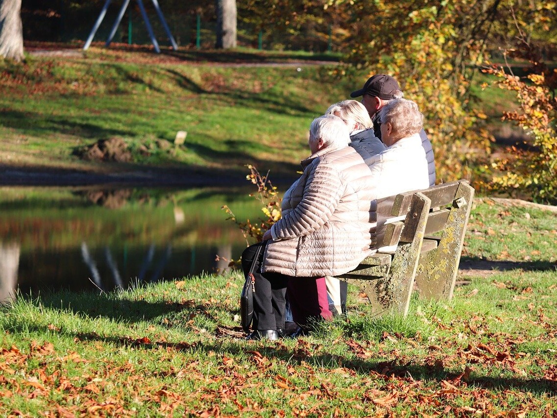 ältere Menschen sitzen auf einer Bak an einem Teich.