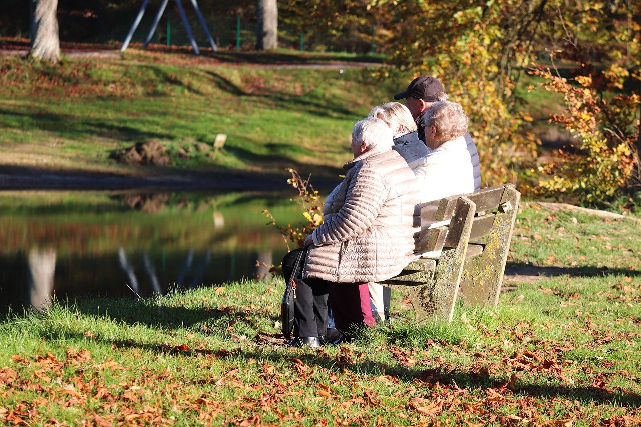 ältere Menschen sitzen auf einer Bak an einem Teich.
